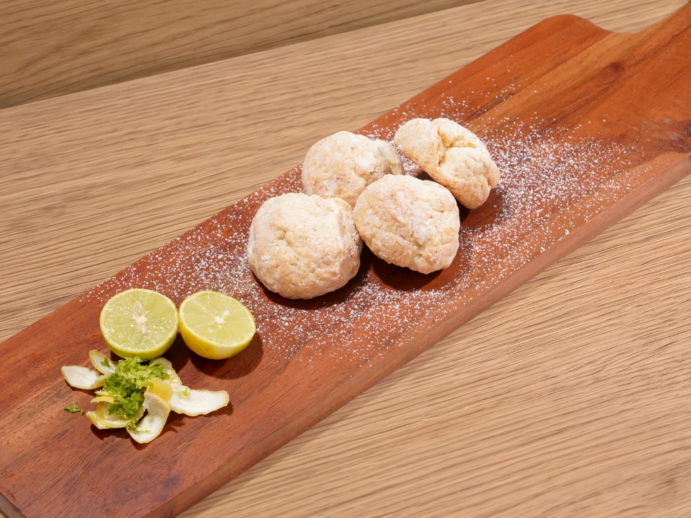Lemon cookies dusted with sugar on a wooden board, with cut limes